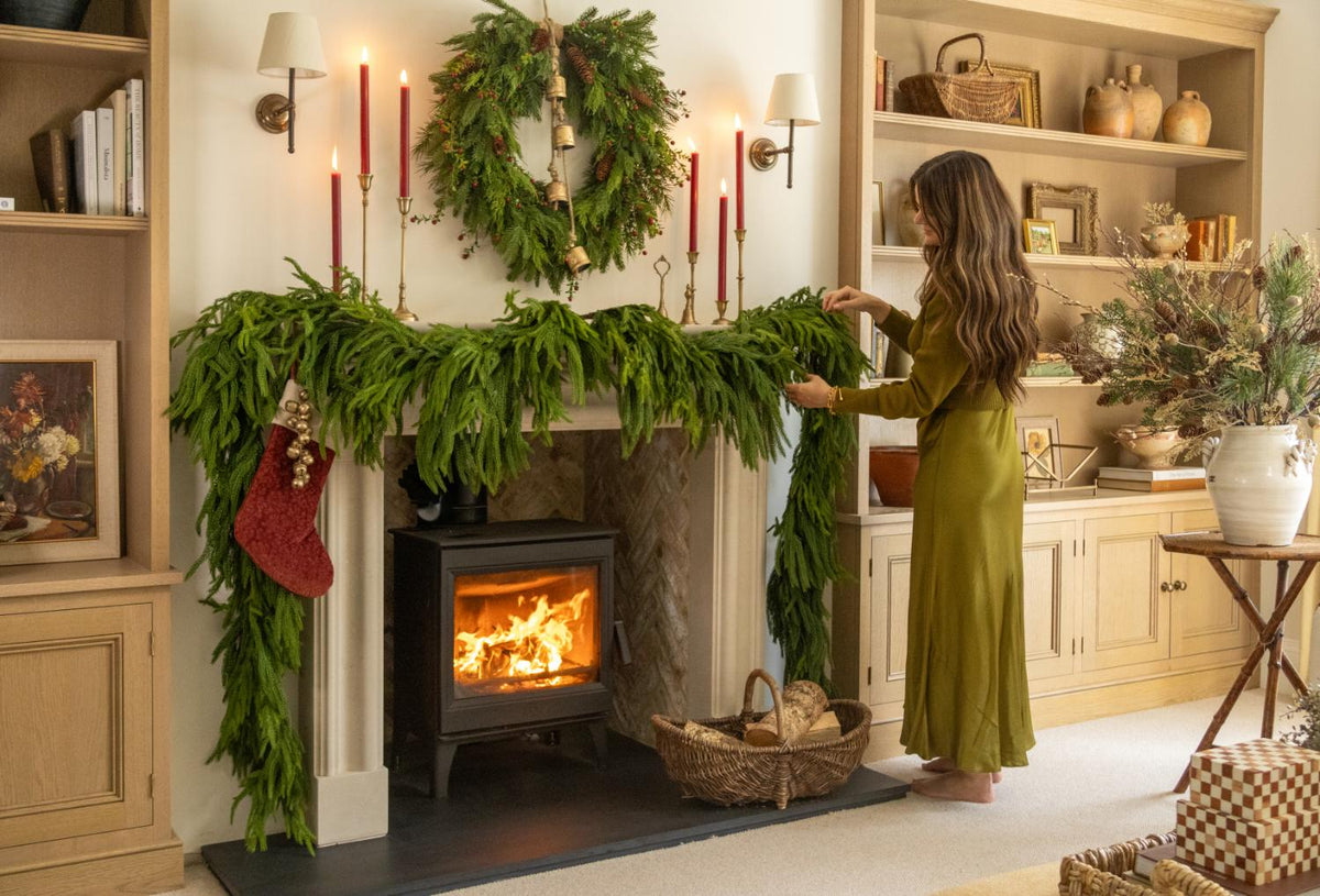 Artificial garlands and wreath styled on a fireplace with lit logburner in a cosy lounge setting 