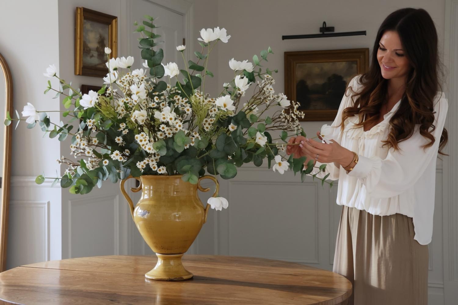 lady arranging large flower arrangement in a yellow vase on a wooden table 