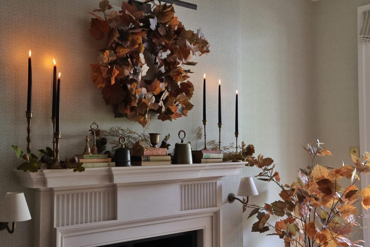 Cosy fireplace scene with candlight, an autumn wreath and brass accessories 