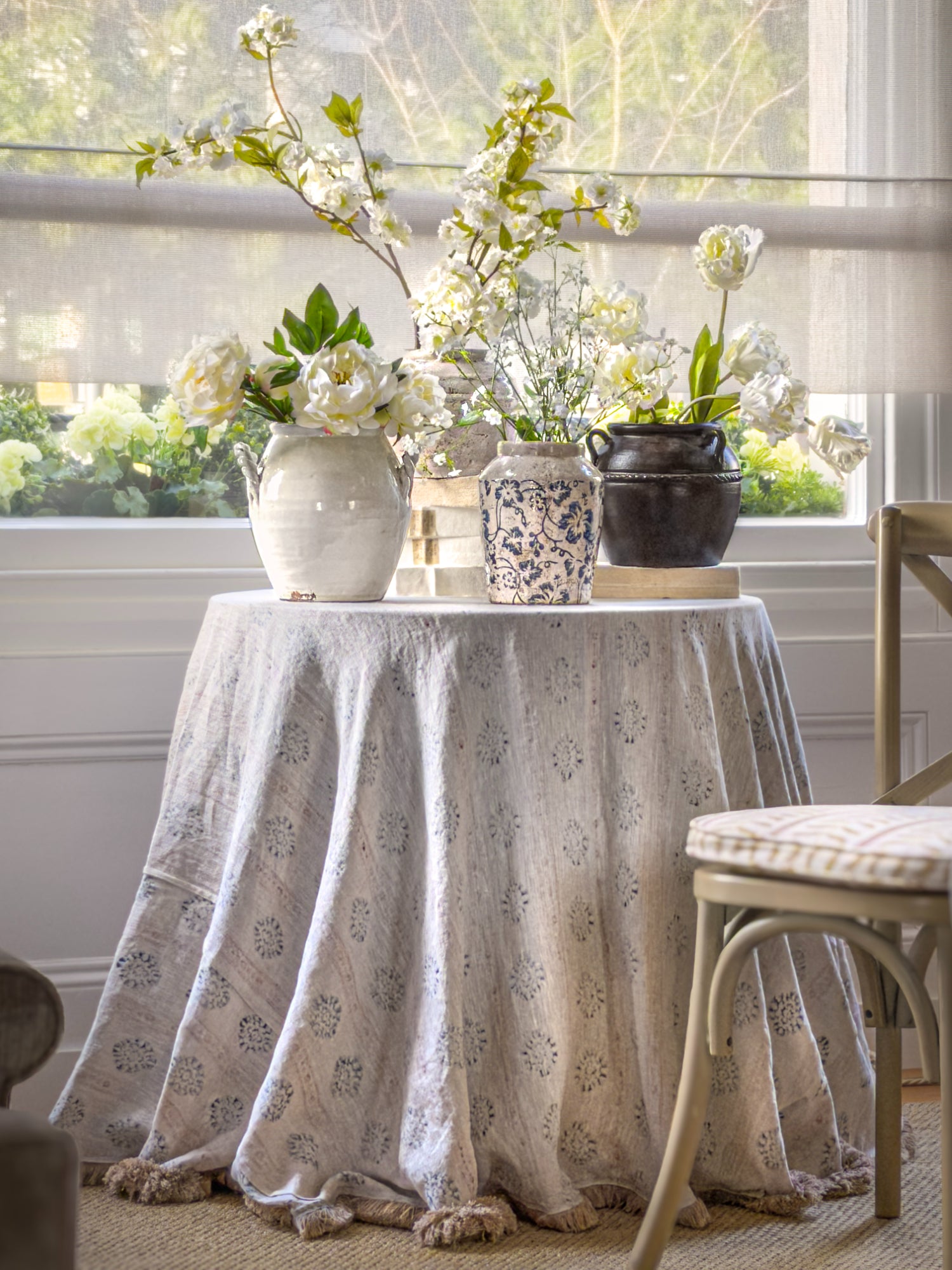 Table with floral arrangements and a patterned tablecloth in a bright room.