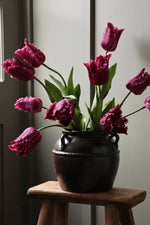 Vase of purple tulips on a wooden stool against a neutral wall