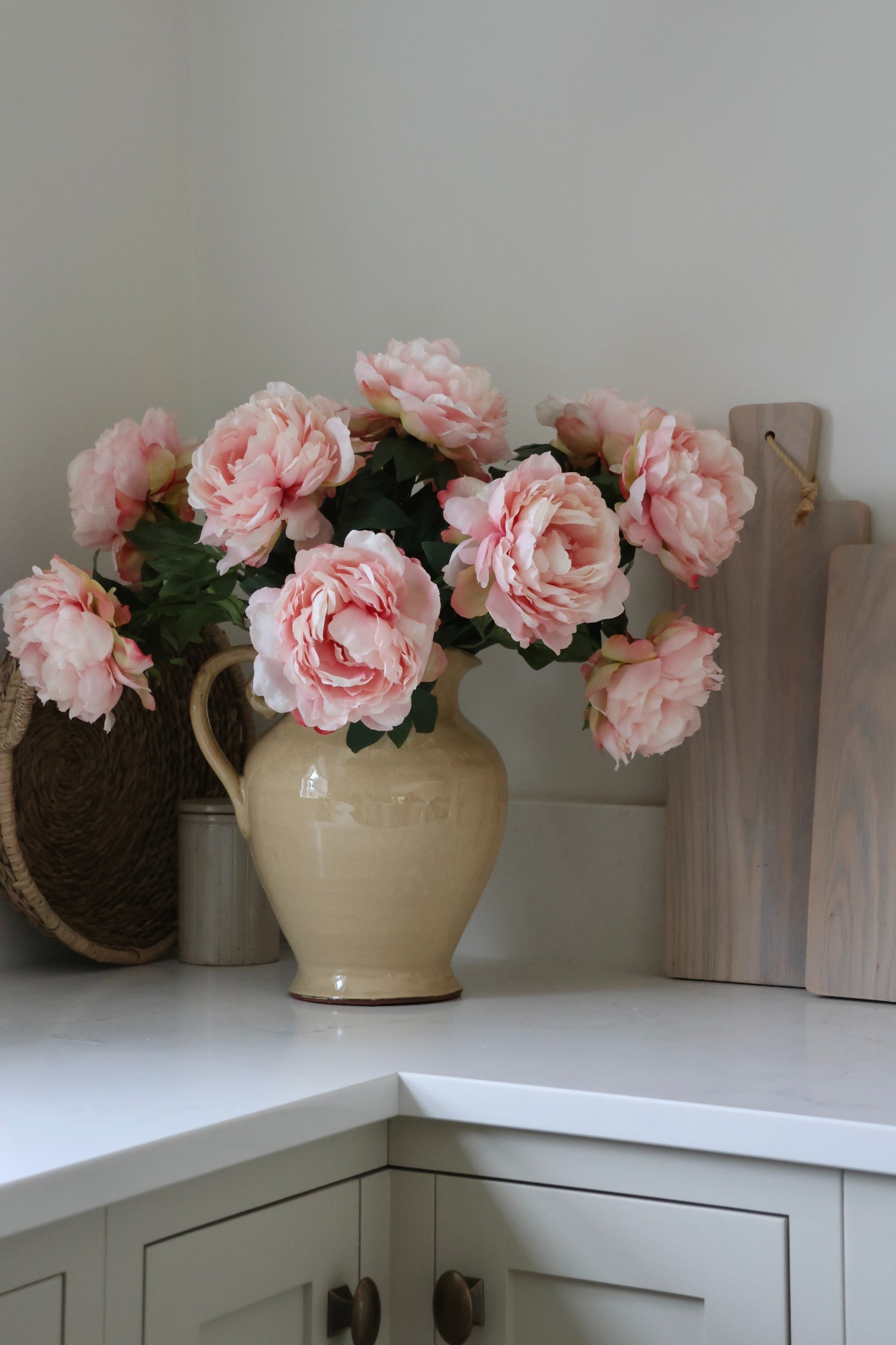 Beige jug with artificial pink peonies on a white kitchen surface
