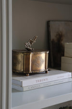 Decorative brass box on top of books with a neutral background