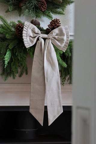 green and white stripe pleated bow hanging from a foliage garland
