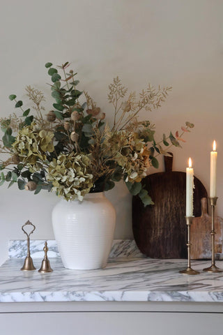 Decorative setup with a vase of flowers, candles, and small accessories on a marble surface.