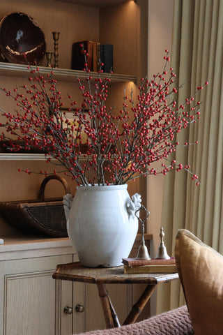 Decorative arrangement of red berries in a white vase on a wooden side table.