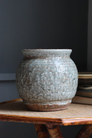 Textured ceramic pot on a wooden surface with a dark background