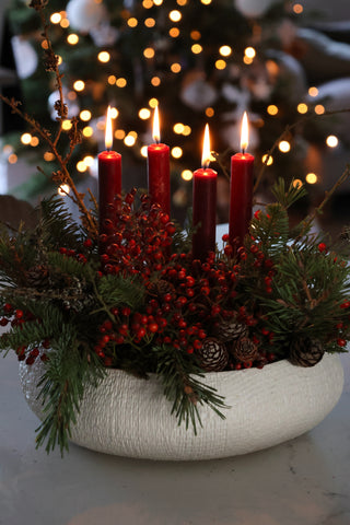 white planter with green foliage, red berries, pine cones and burgundy candles 
