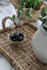 woven banana bark tray styled with bowl of figs and ceramic vase with eucalyptus in kitchen setting
