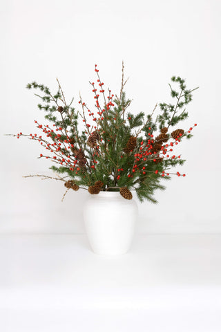 Artificial flower arrangement green foliage, red berries in white vase on white background