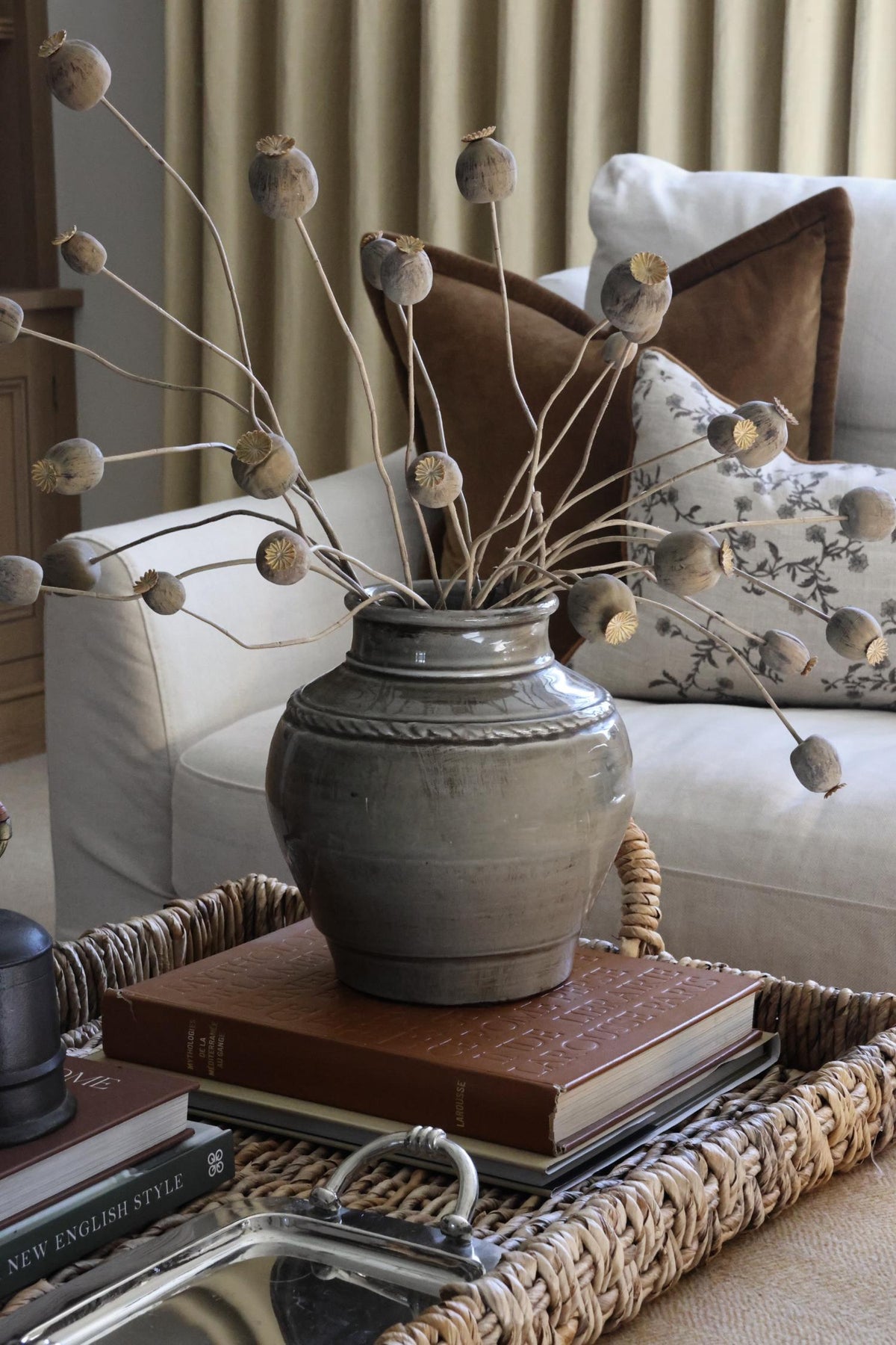 Artificial dried poppy branches styled in a grey ceramic vase on a styled coffee table in a cosy living room setting
