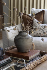 Artificial dried poppy branches styled in a grey ceramic vase on a styled coffee table in a cosy living room setting