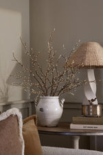 Artificial Willow Spray in white rustic Ceramic vase on a wooden side table with lamp 