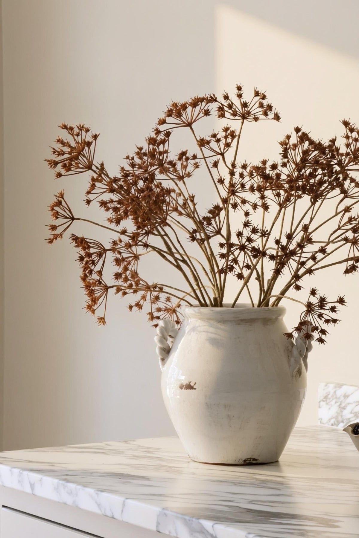 Autumn artificial floral arrangement in a white ceramic vase on a marble worktop 