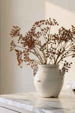 Autumn artificial floral arrangement in a white ceramic vase on a marble worktop 