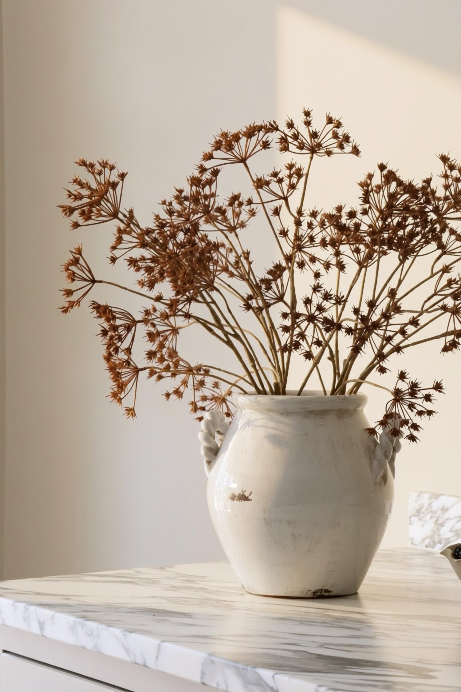 Autumn artificial floral arrangement in a white ceramic vase on a marble worktop 