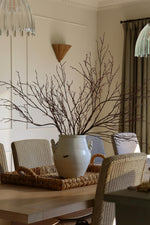 Artificial birch branches in large white vase on a rattan tray in a dininy room setting 