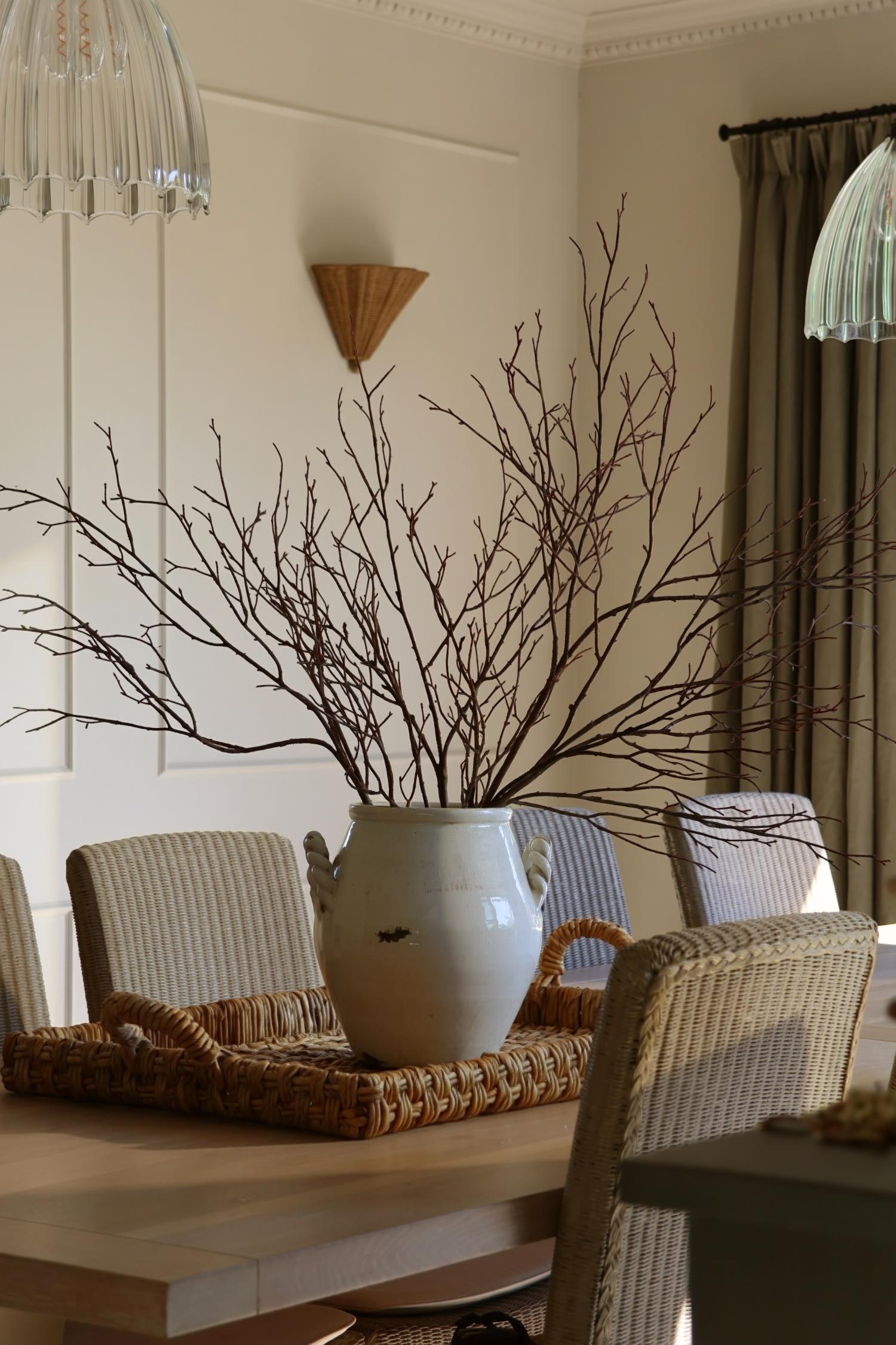 Artificial birch branches in large white vase on a rattan tray in a dininy room setting 