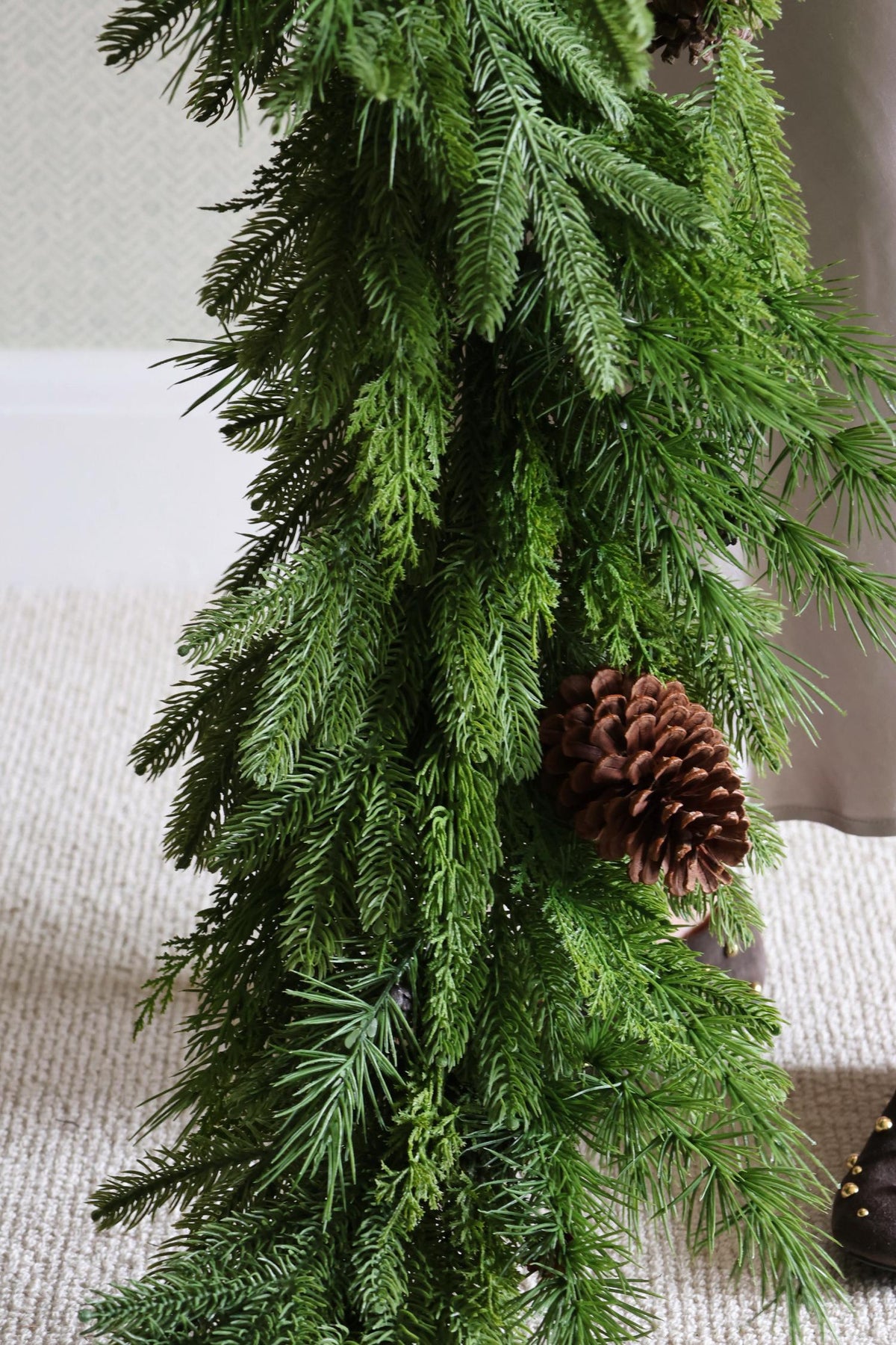 Artificial green garland with a pine cone on a neutral background