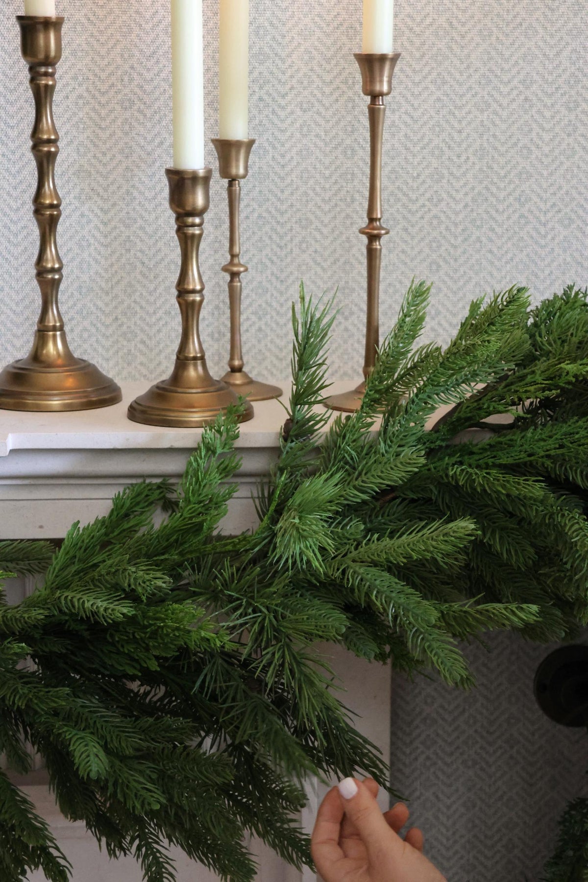Decorative faux garland with candles in brass candlesticks on a textured wall background