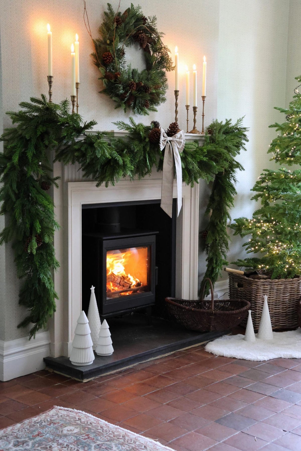 Cosy fireplace dressed with artificial faux Christmas garlands, wreaths, decorations, and a christmas tree.