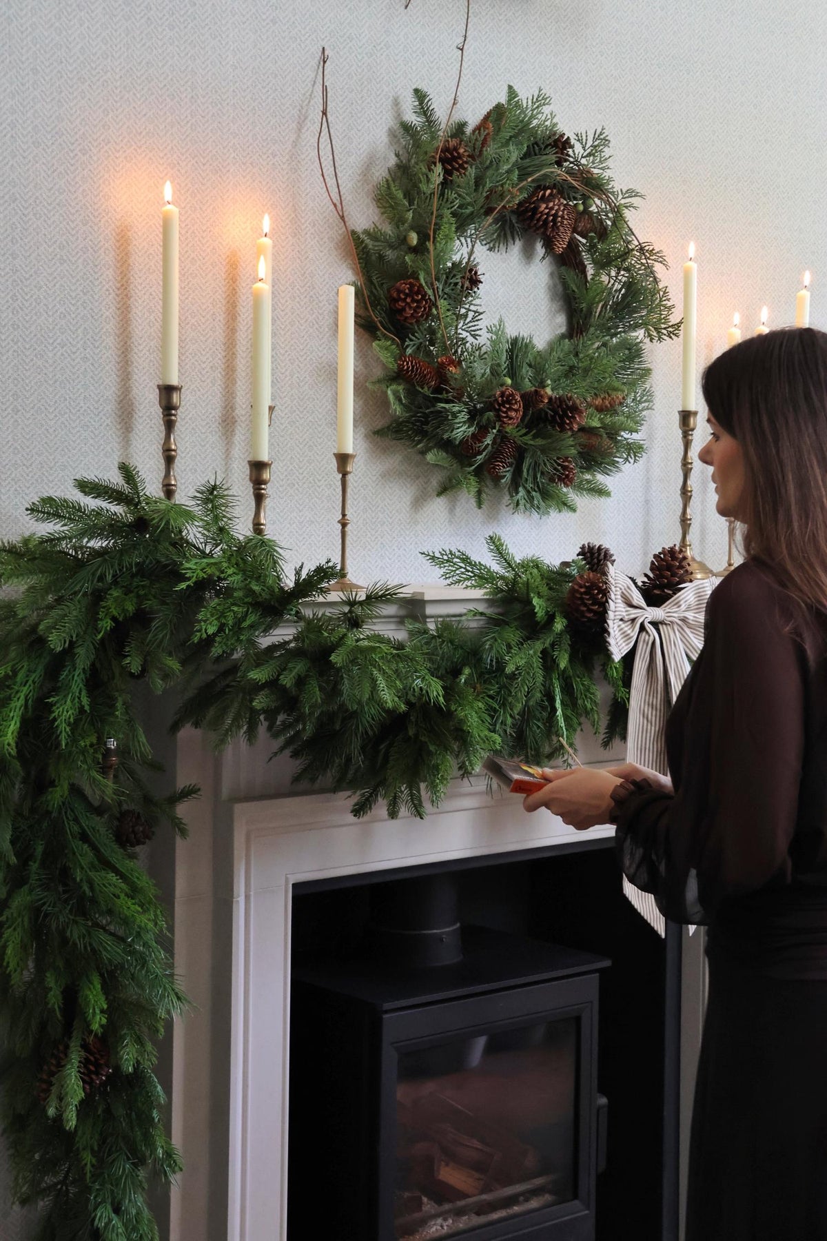 Woman standing in front of a fireplace decorated with artificial garlands, a wreath and candles