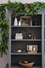 Decorative shelf with festive greenery and holiday decor against a gray wall.