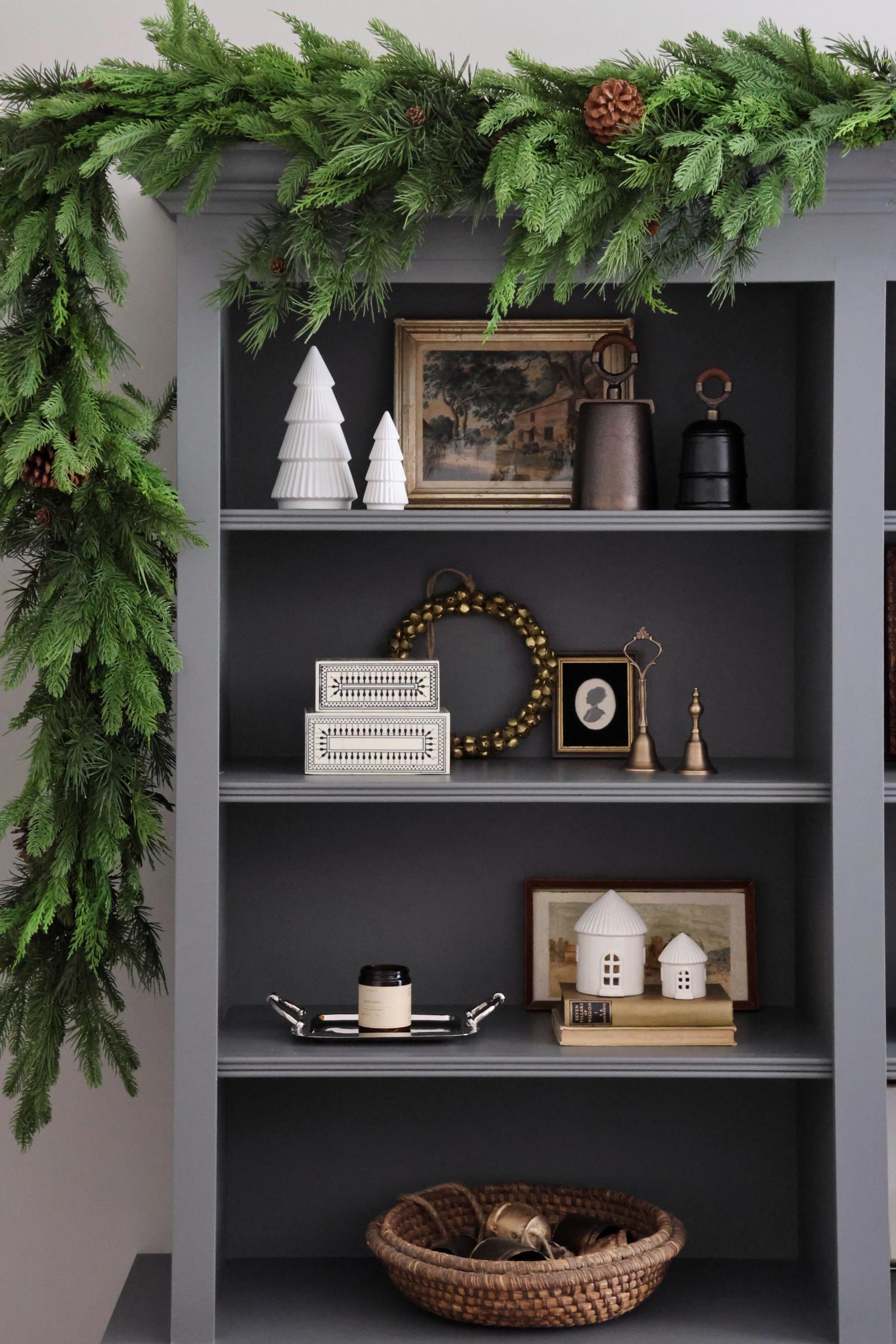 Decorative shelf with festive greenery and holiday decor against a gray wall.