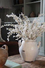 Artificial white willow stems in a rustic white ceramic vase on a wooden coffee table 
