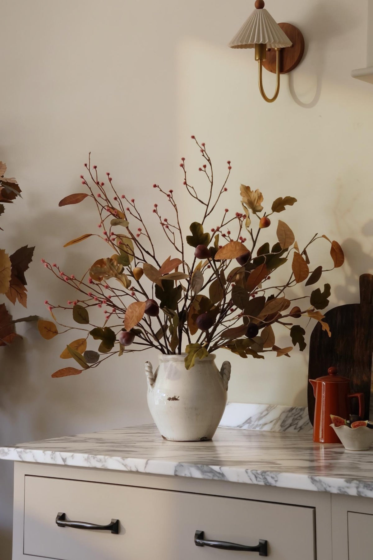 Artificial autumn arrangement in a white ceramic vase on a marble kitchen island 