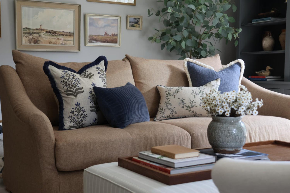 Blue decorative pillows styled on a brown sofa with large tree and art in the background and coffee table in the foreground