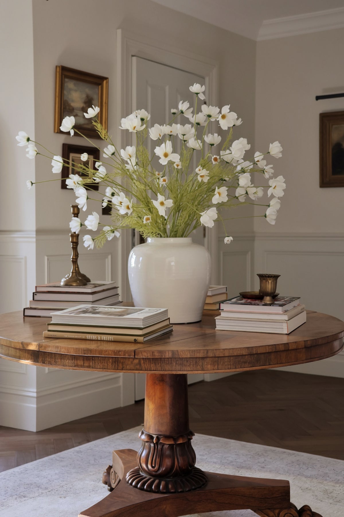 large wooden round table with white vase and big flower arrangement of cosmos