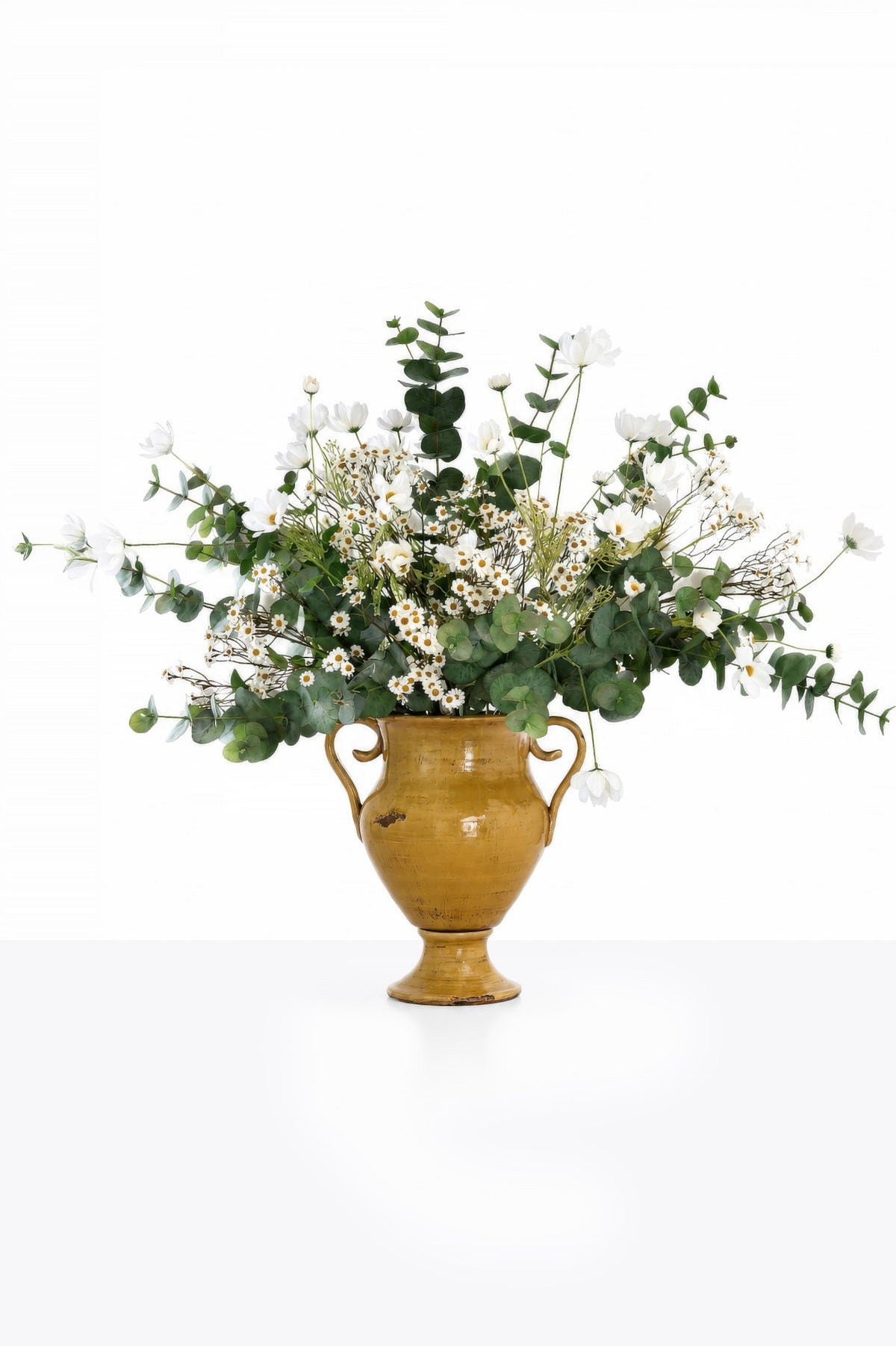 Faux daisy and green eucalyptus arrangement in yellow vase on white background 