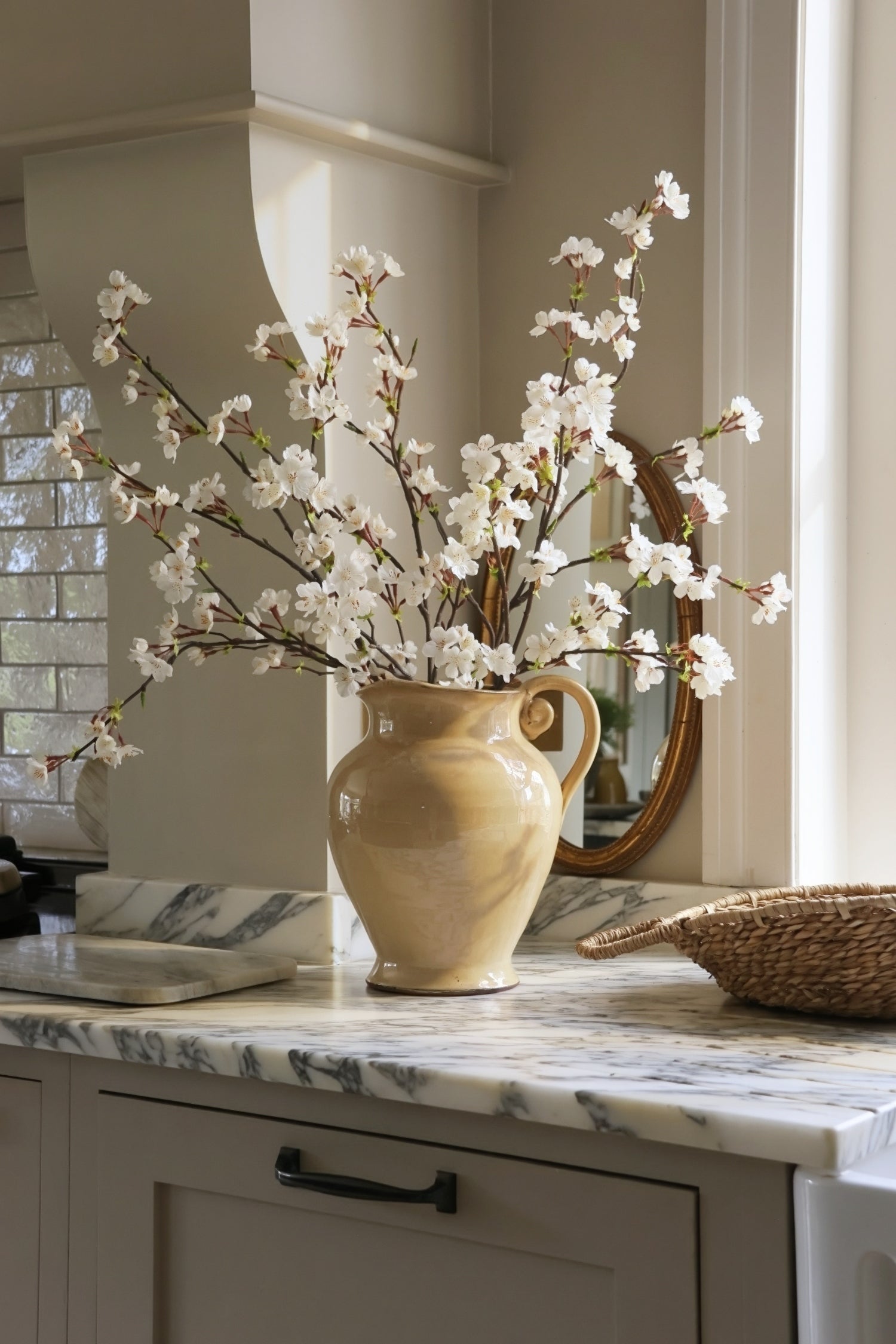 Decorative jug with white floral blossom on a kitchen counter.