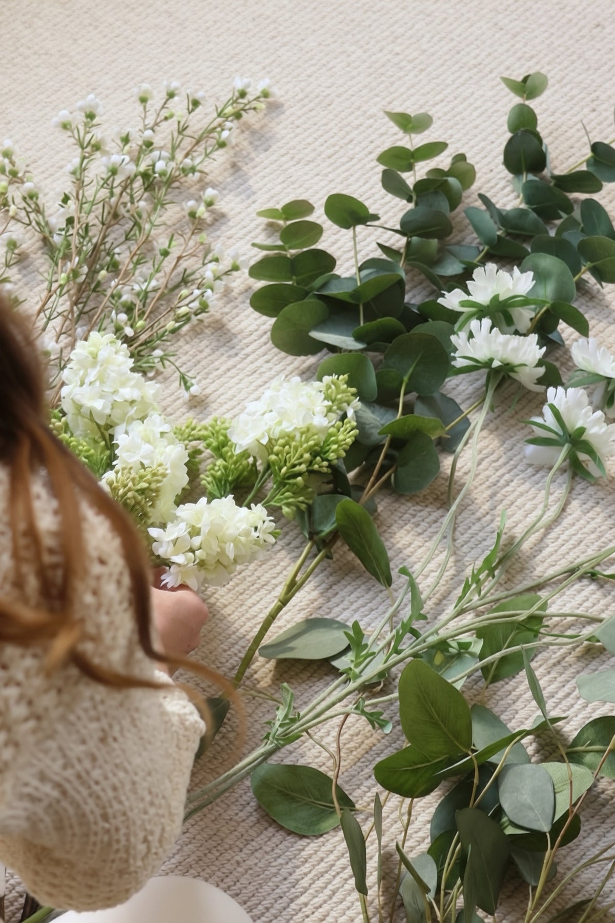 Person arranging greenery and white flowers on a textured surface