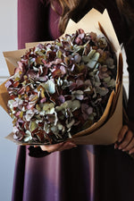 Large bouquet of Faux Mulberry hydrangeas wrapped in brown paper held by women in purple dress 