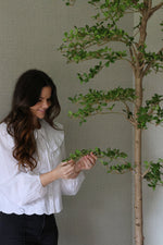 Woman tending to an artificial shady lady tree against a plain wall