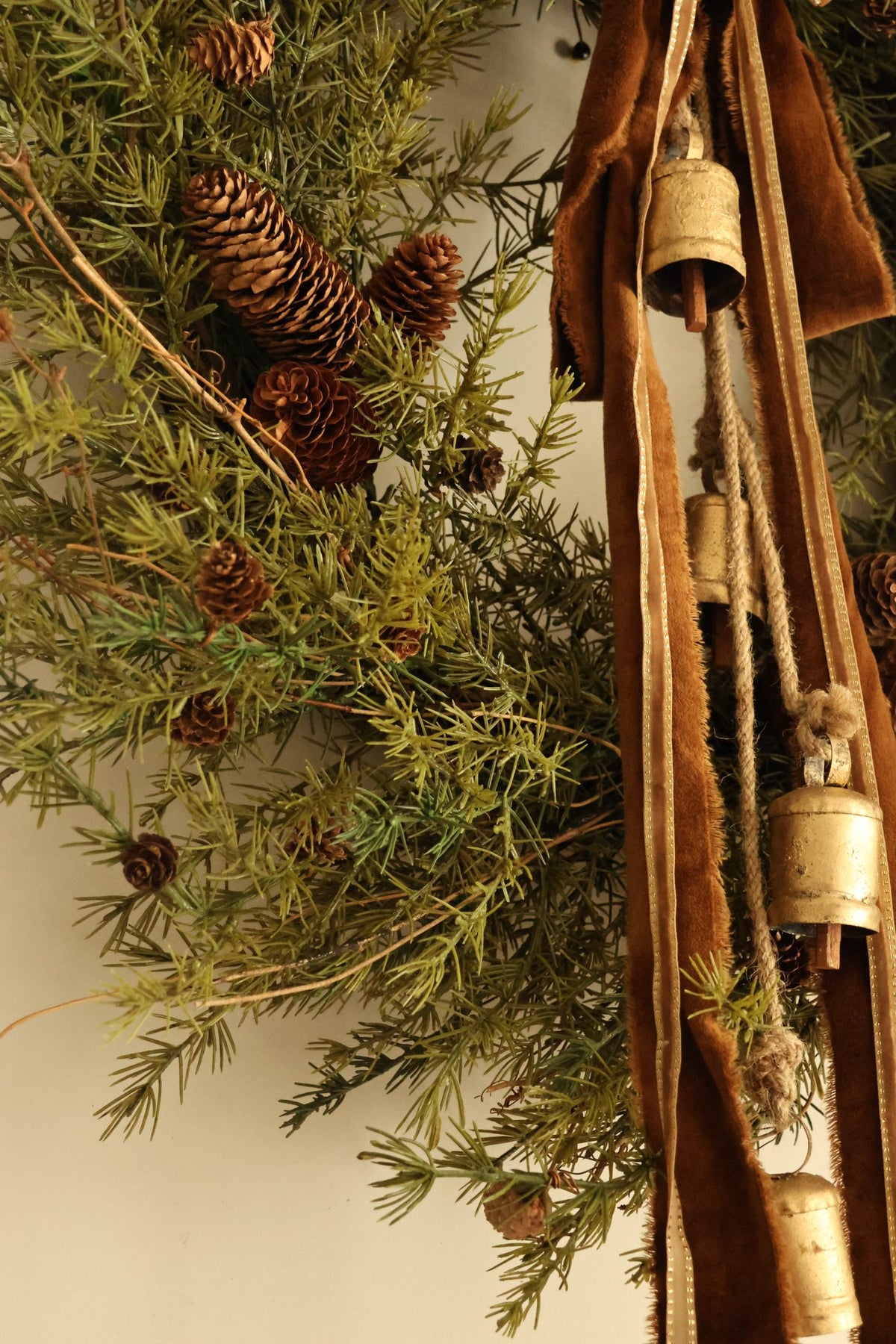Close up of artificial larix style foliage with velvet ribbons and brass cowbells on plain background 