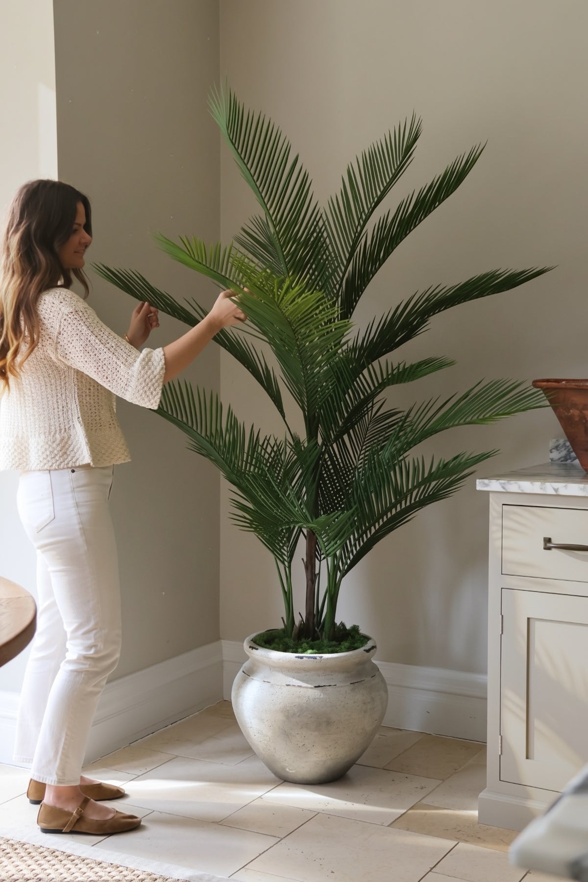 Faux palm tree 180cm in ultra-lite barrown planter in kitchen with lady arranging the leaves 