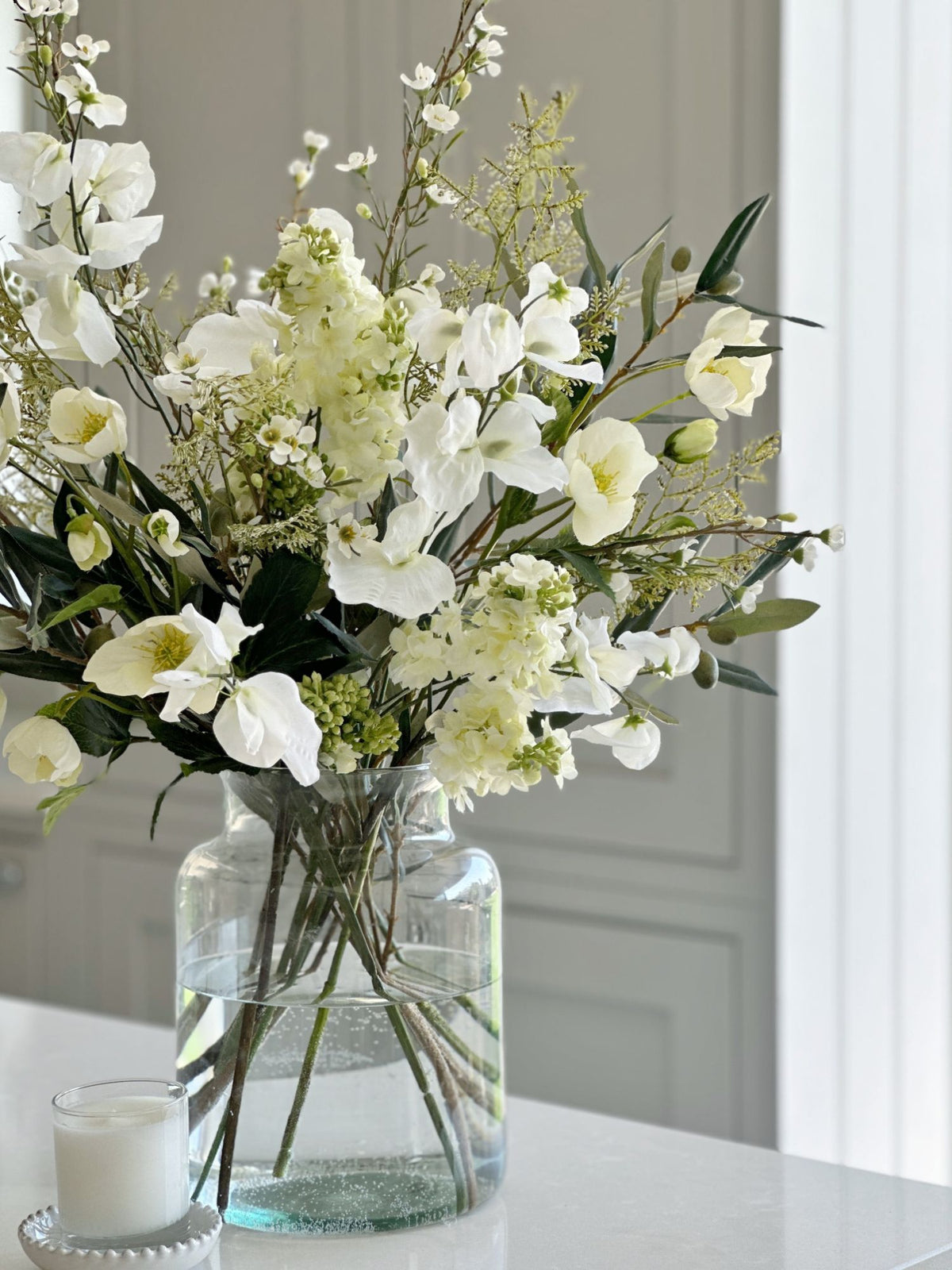 Faux white and green flower arrangement in a glass vase with water