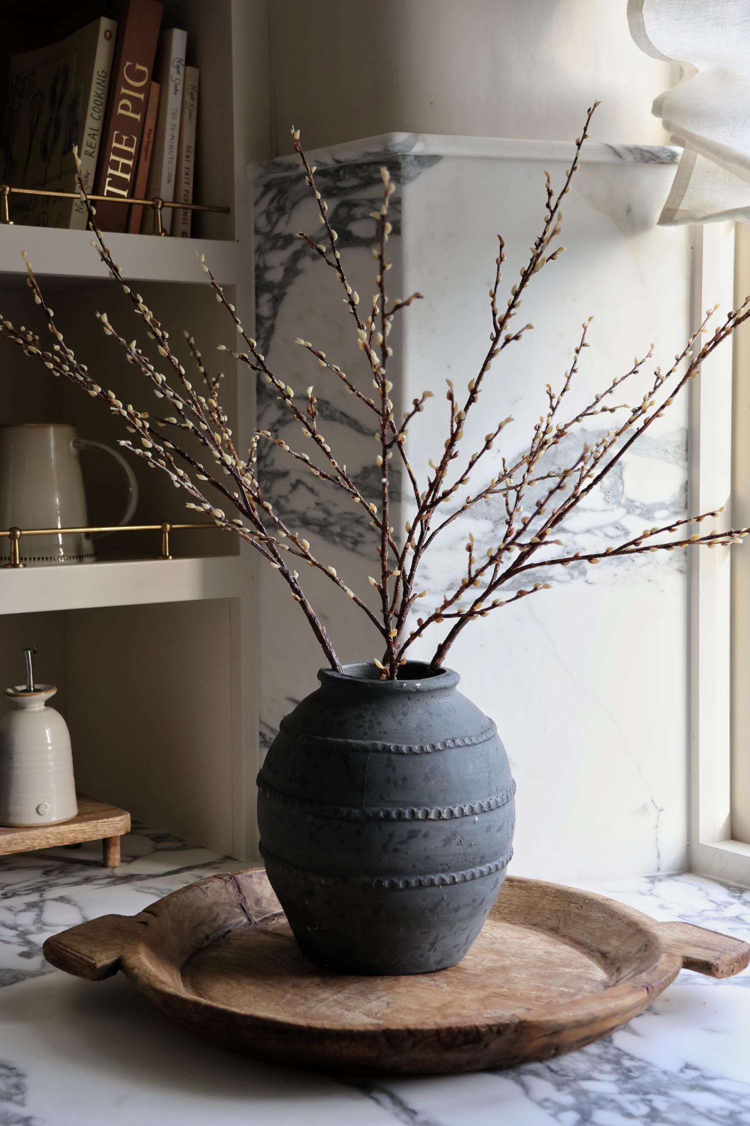 A faux willow spray with lifelike off-white buds on varying sized branches, arranged in a rustic style vase.