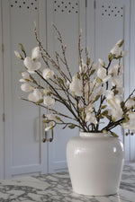 Faux willow spray with magnolia in white vase on marble