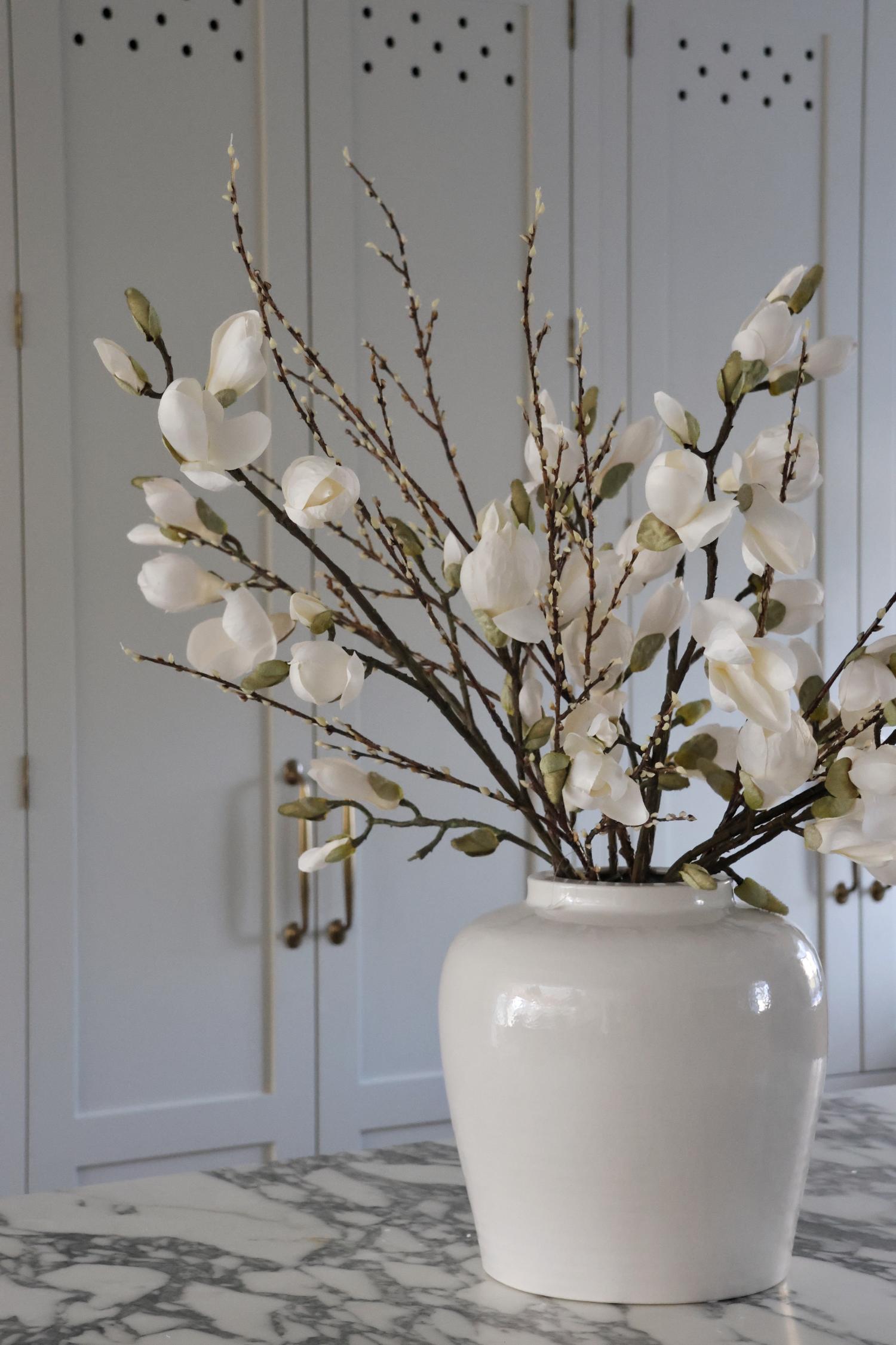 Faux willow spray with magnolia in white vase on marble