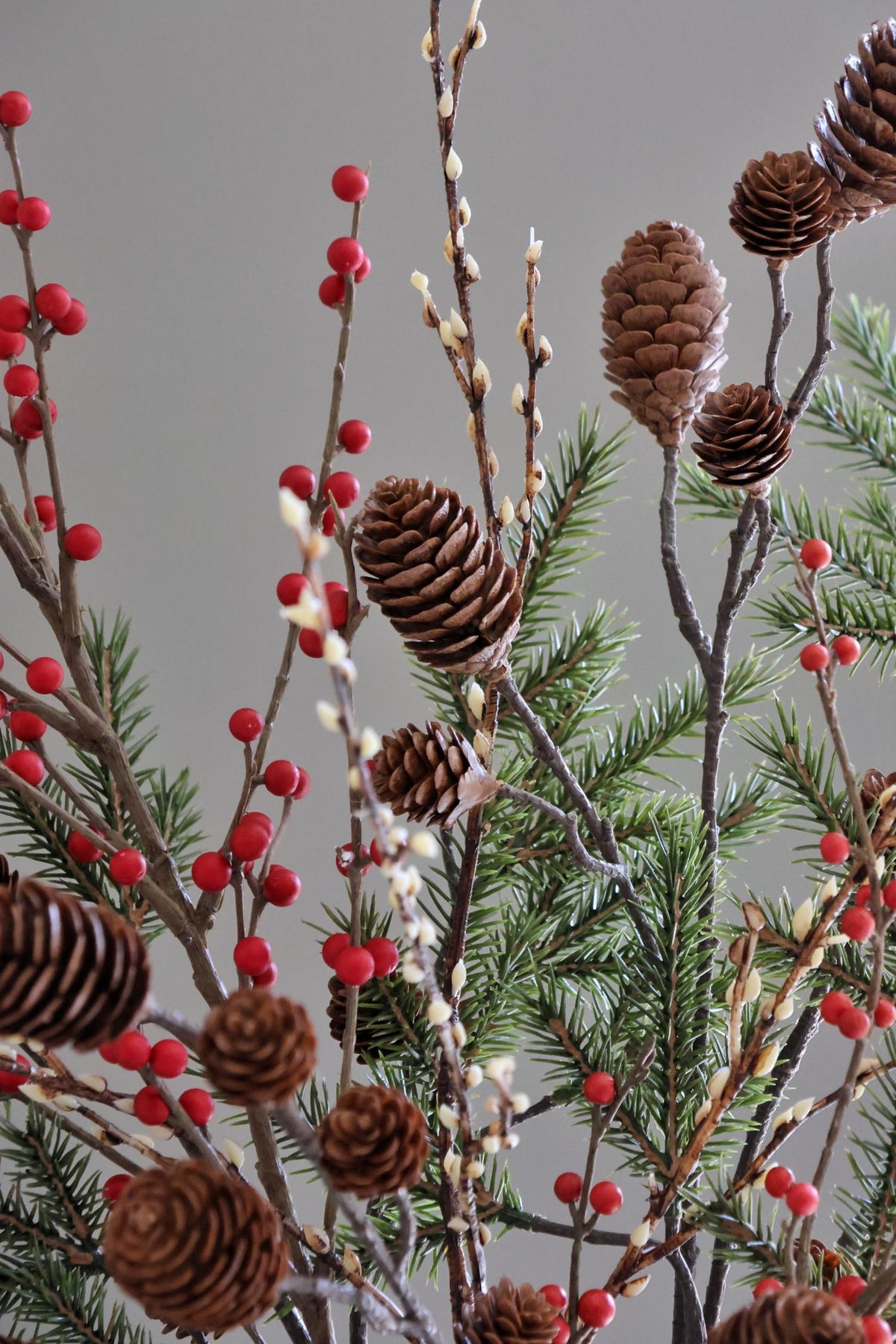 Decorative arrangement with pine cones, red berries, and greenery on a gray background