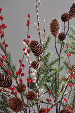 Decorative arrangement with pine cones, red berries, and greenery on a gray background