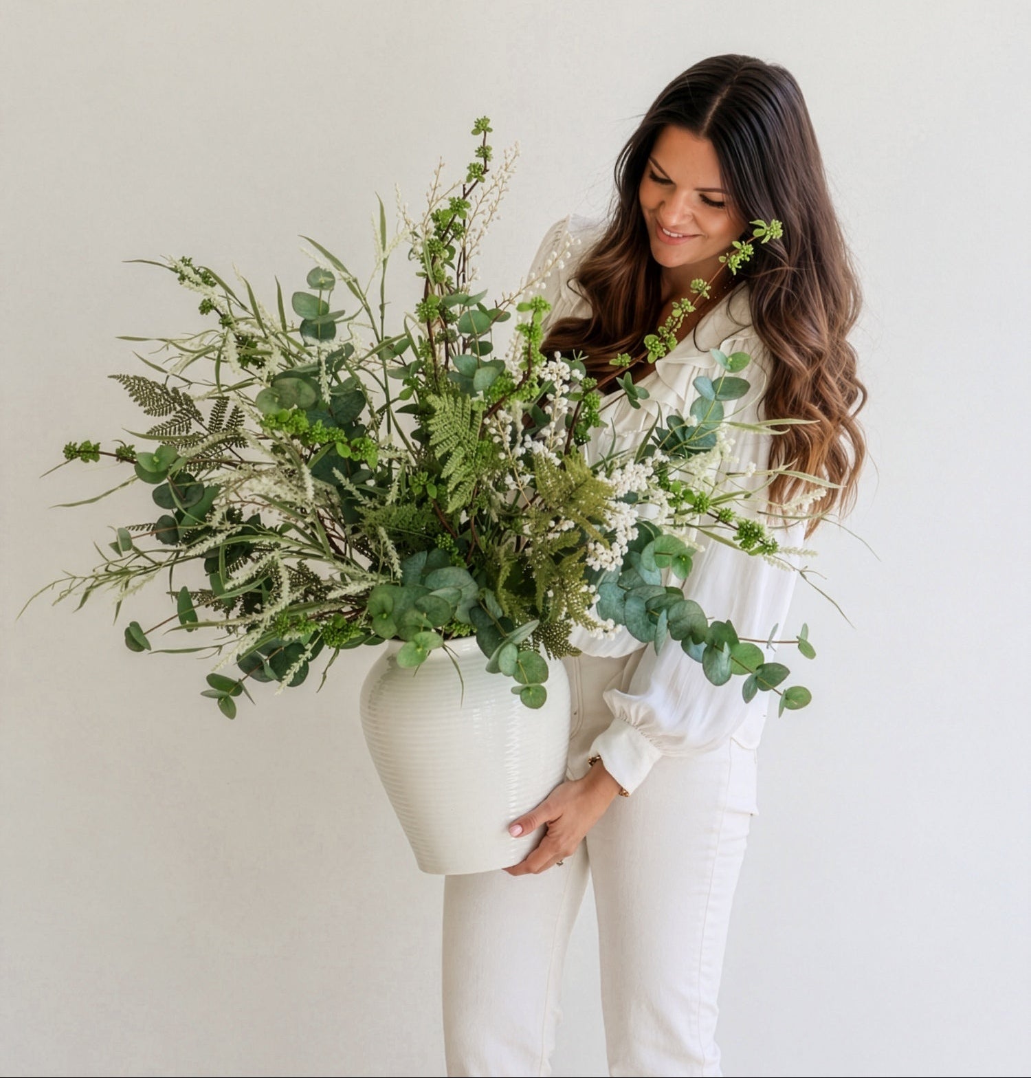 Lady holding white vase with large green faux foliage arrangement
