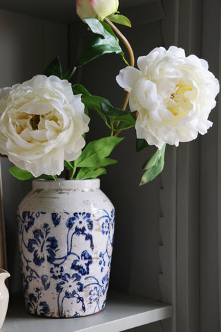 White flowers in a blue and white patterned vase on a shelf.