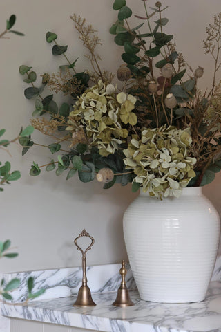 White vase with green flowers on a marble surface