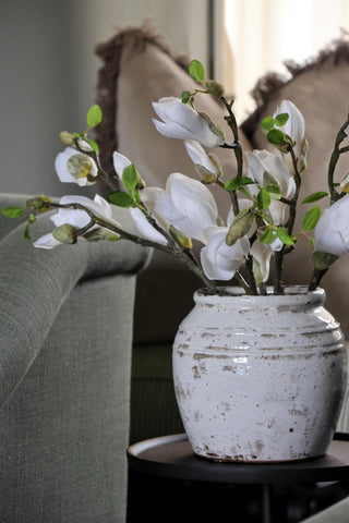 White flowers in a rustic vase on a table with a blurred background