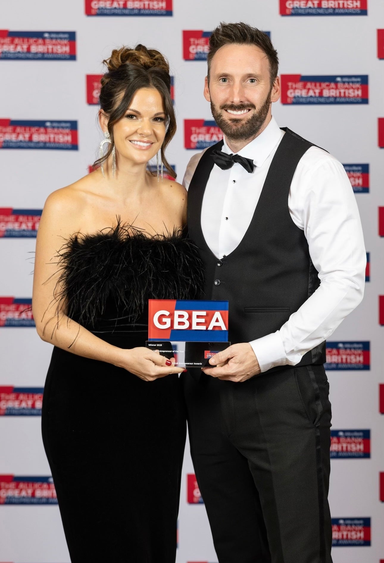 Man and woman holding an award with GBEA logo against a branded background